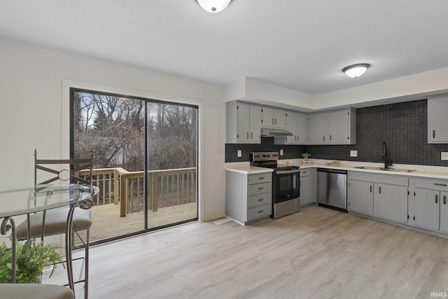 kitchen with light wood finished floors, stainless steel appliances, gray cabinetry, under cabinet range hood, and a sink