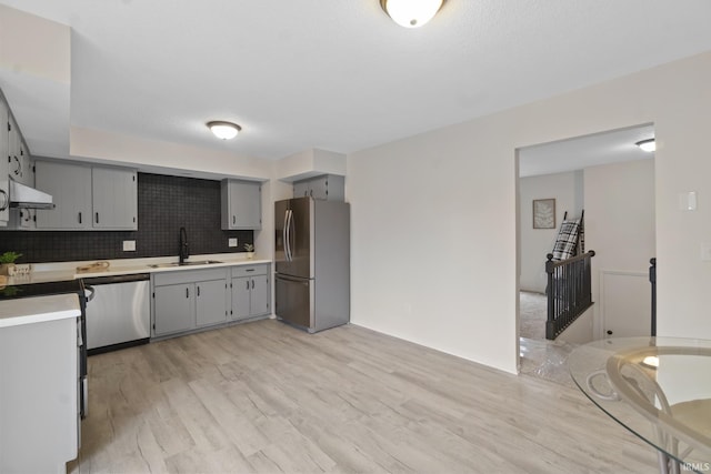 kitchen featuring appliances with stainless steel finishes, light countertops, gray cabinetry, under cabinet range hood, and a sink