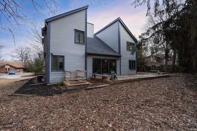 back of house at dusk featuring a shingled roof, a wooden deck, and central air condition unit