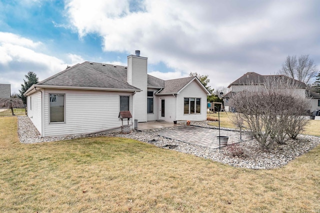 back of property with a shingled roof, a patio area, a lawn, and a chimney