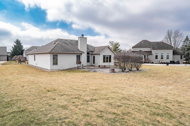 rear view of property featuring roof with shingles, a chimney, a patio area, and a lawn