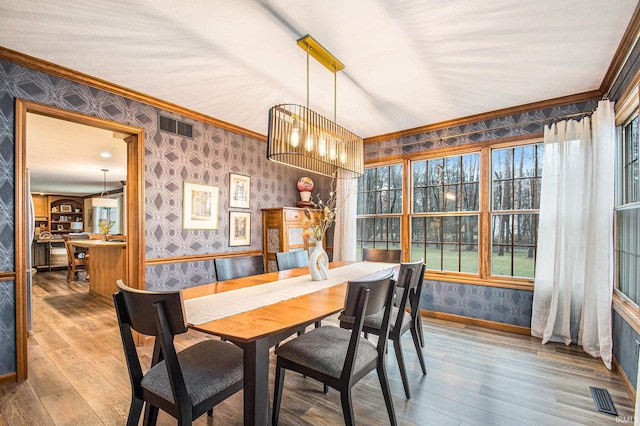 dining room featuring ornamental molding, wood finished floors, visible vents, and wallpapered walls