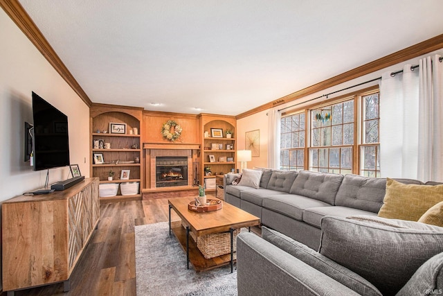 living room with built in shelves, a tiled fireplace, dark wood finished floors, and crown molding