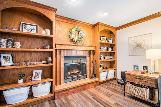 living area with built in shelves, a fireplace, wood finished floors, and crown molding