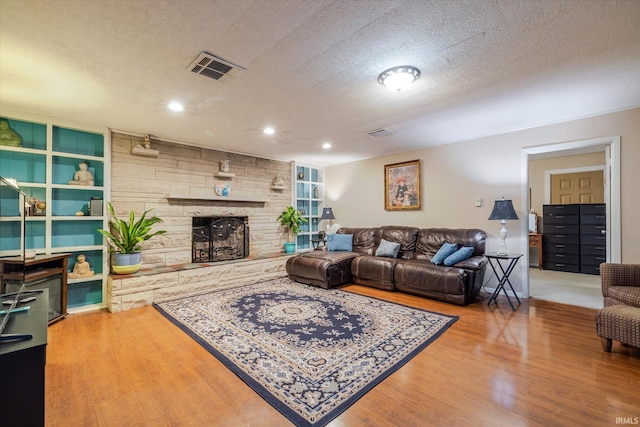 living area featuring a textured ceiling, visible vents, a fireplace, and wood finished floors