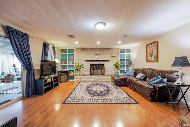 living area featuring built in shelves, visible vents, a textured ceiling, and wood finished floors