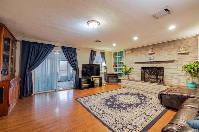 living area featuring a textured ceiling, a stone fireplace, wood finished floors, and visible vents