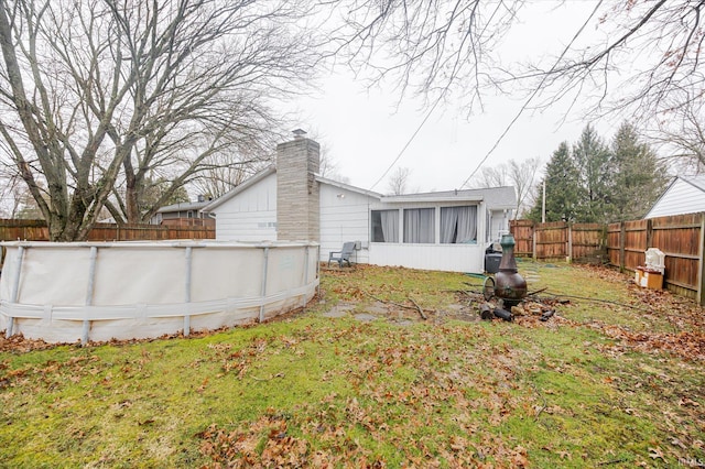 back of property with a fenced in pool, a chimney, a lawn, a sunroom, and a fenced backyard