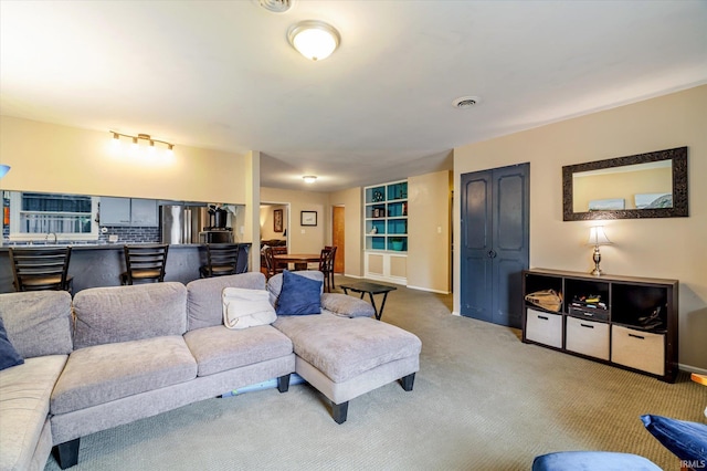 living area with baseboards, visible vents, and light colored carpet