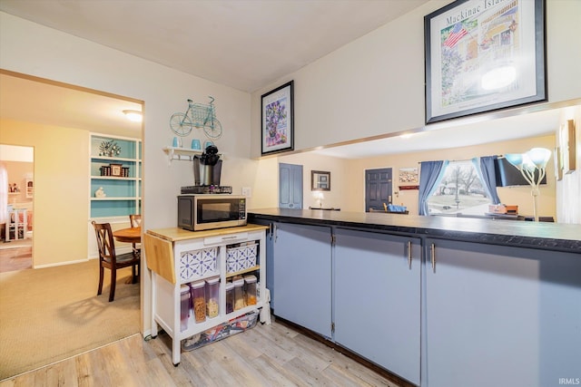 kitchen featuring light wood-type flooring, stainless steel microwave, and dark countertops