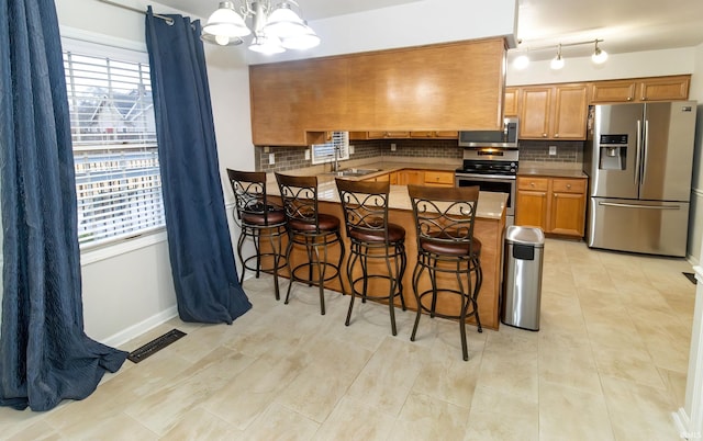 kitchen with brown cabinets, tasteful backsplash, visible vents, appliances with stainless steel finishes, and a peninsula