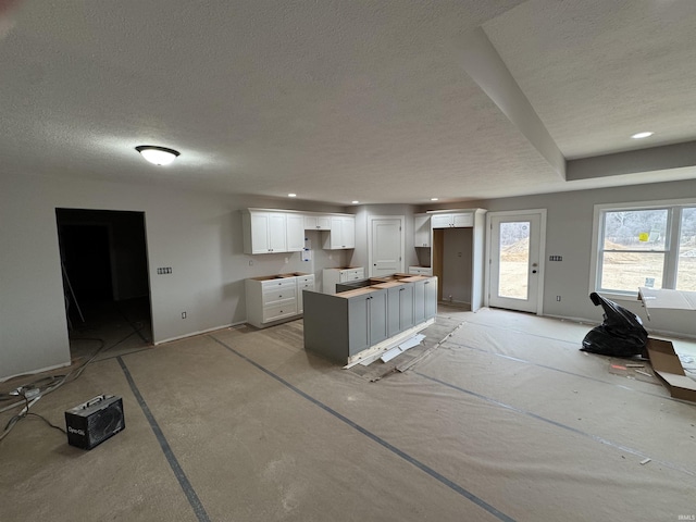 kitchen featuring recessed lighting, white cabinetry, a kitchen island, a textured ceiling, and baseboards