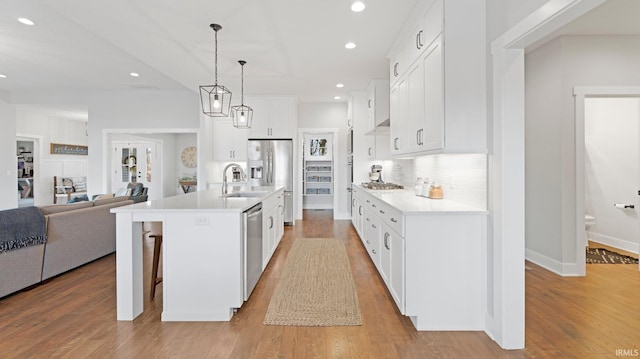 kitchen with light wood finished floors, decorative backsplash, open floor plan, stainless steel appliances, and light countertops