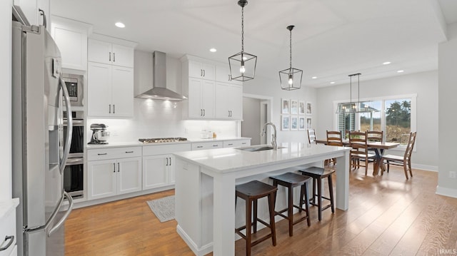 kitchen with stainless steel refrigerator with ice dispenser, backsplash, a sink, gas cooktop, and wall chimney exhaust hood