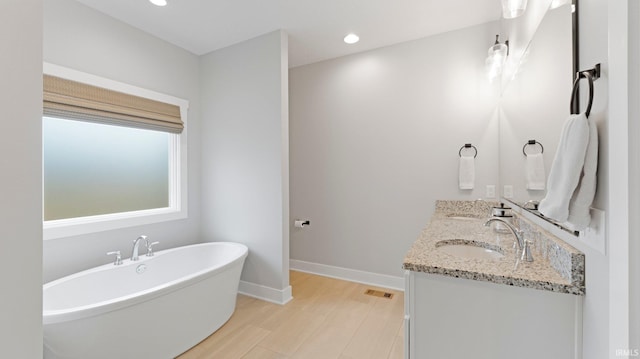 bathroom with a freestanding tub, wood finished floors, a sink, baseboards, and double vanity