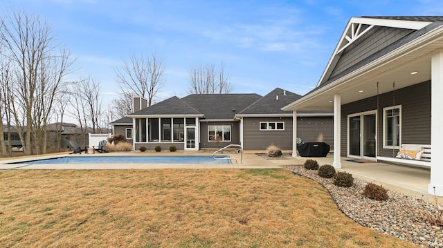 rear view of property featuring a sunroom, a patio area, a lawn, and a chimney