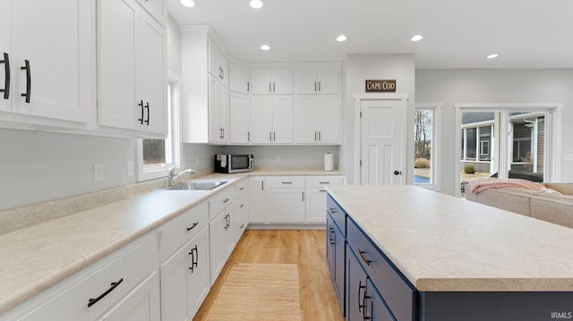 kitchen featuring blue cabinetry, light countertops, stainless steel microwave, white cabinets, and a sink