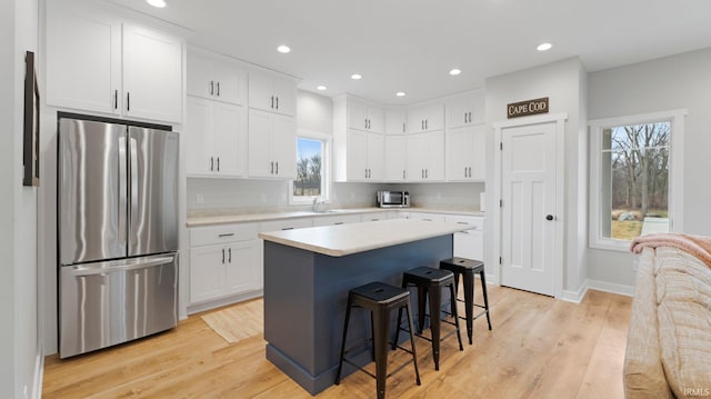 kitchen featuring white cabinets, freestanding refrigerator, light countertops, a kitchen bar, and a sink