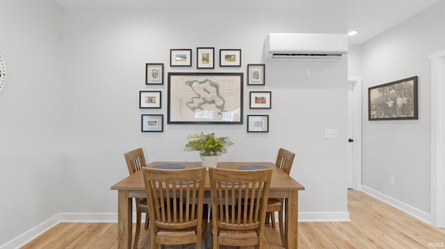 dining room with a wall unit AC, light wood-style flooring, and baseboards