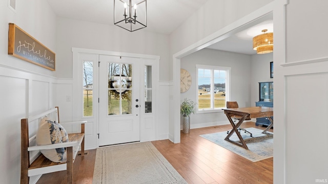 entrance foyer with a wainscoted wall, a notable chandelier, visible vents, a decorative wall, and wood finished floors