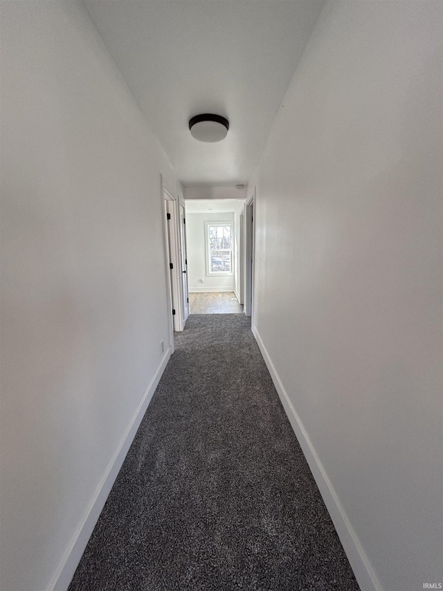 hall with baseboards and dark colored carpet