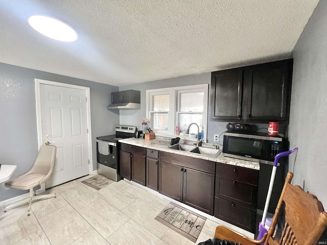 kitchen with stainless steel appliances, dark brown cabinetry, a sink, a textured ceiling, and baseboards