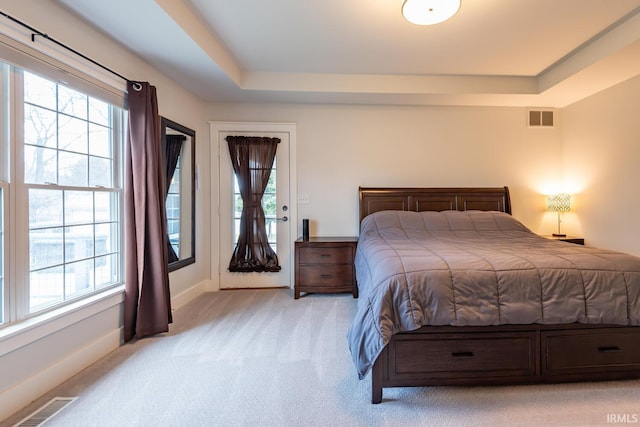 bedroom with a raised ceiling, visible vents, and light colored carpet