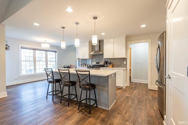 kitchen featuring a kitchen breakfast bar, light countertops, appliances with stainless steel finishes, wall chimney range hood, and backsplash