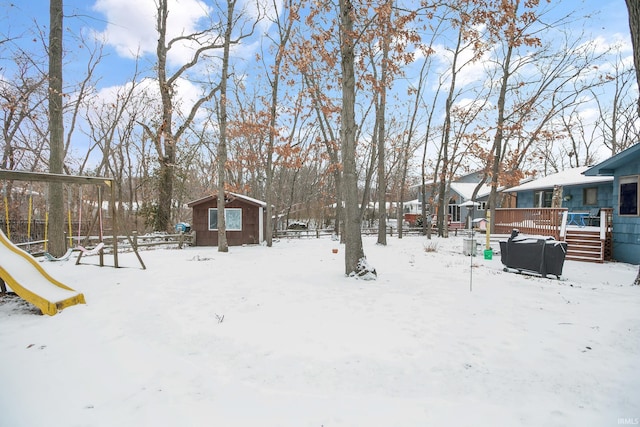 snowy yard featuring an outdoor structure, a playground, and a wooden deck