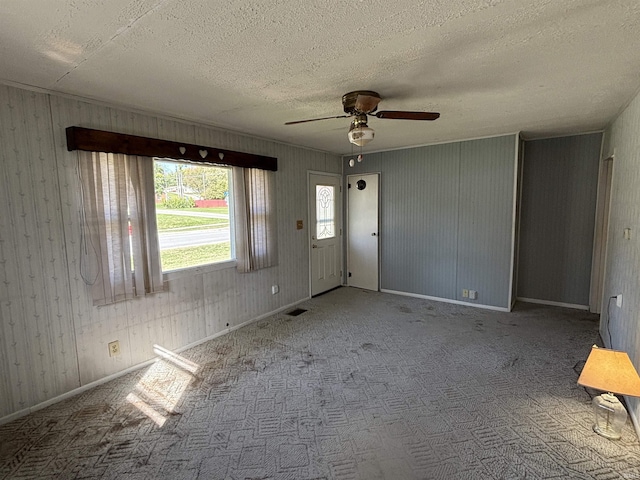 carpeted empty room with a textured ceiling, a ceiling fan, visible vents, and baseboards