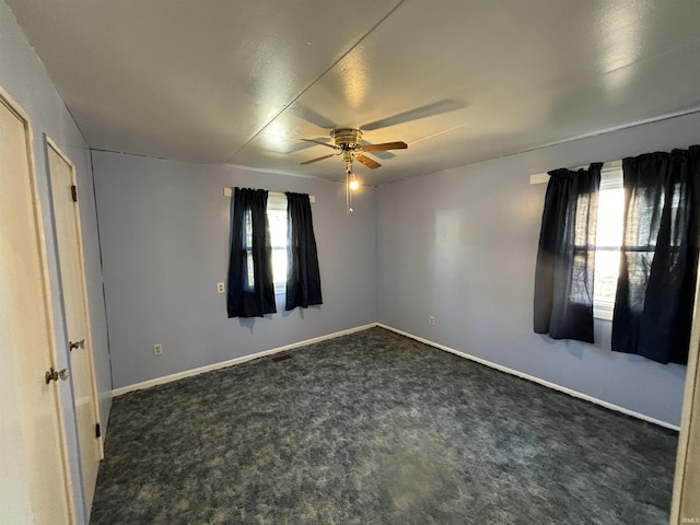 empty room with ceiling fan, dark colored carpet, and baseboards