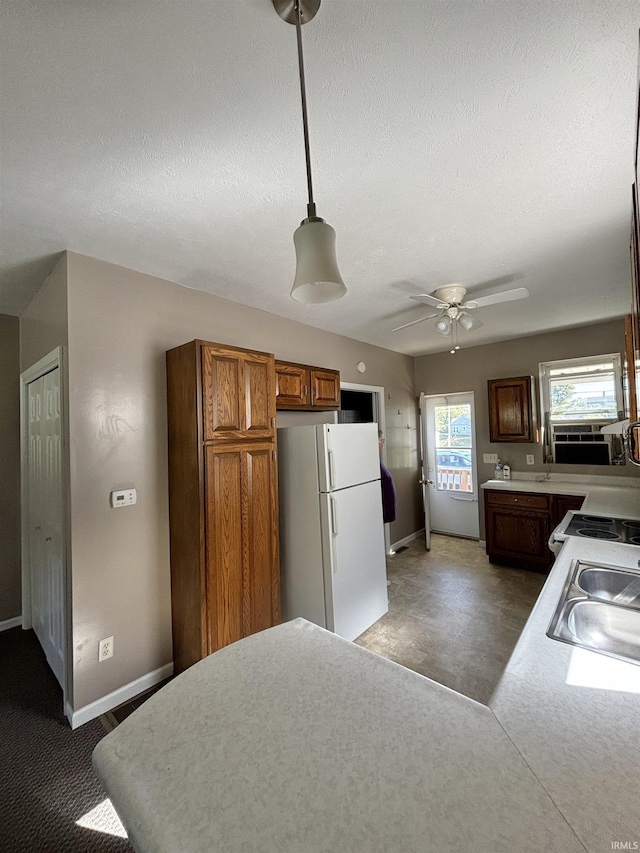 kitchen featuring brown cabinetry, freestanding refrigerator, light countertops, a textured ceiling, and a sink