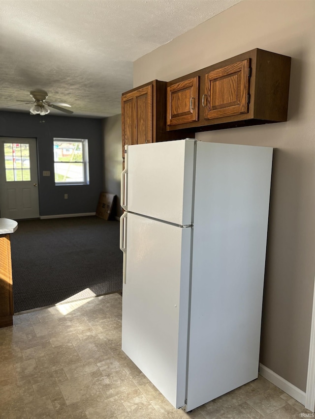 kitchen featuring a textured ceiling, a ceiling fan, baseboards, freestanding refrigerator, and brown cabinetry