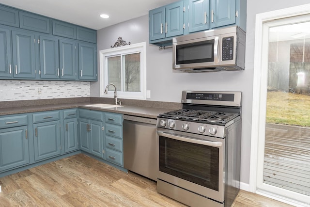 kitchen featuring dark countertops, appliances with stainless steel finishes, a sink, blue cabinets, and light wood-type flooring