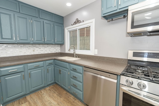 kitchen with dark countertops, stainless steel appliances, light wood-type flooring, blue cabinetry, and a sink