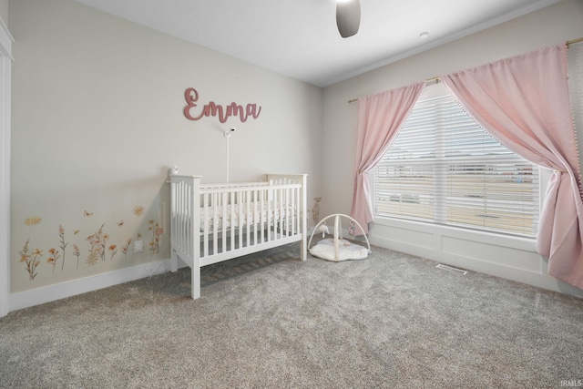 unfurnished bedroom featuring carpet floors, visible vents, ceiling fan, a crib, and baseboards