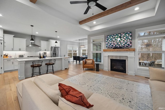 living room with a ceiling fan, a glass covered fireplace, beamed ceiling, light wood-type flooring, and recessed lighting