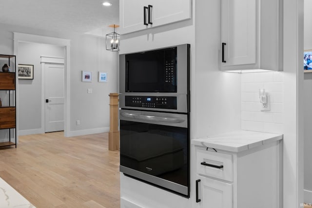 kitchen with decorative backsplash, light wood-style flooring, oven, light stone countertops, and white cabinetry