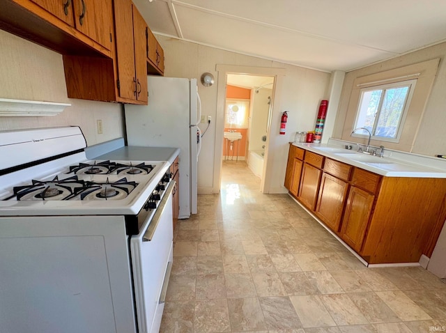 kitchen featuring white range with gas cooktop, brown cabinetry, a sink, and light countertops