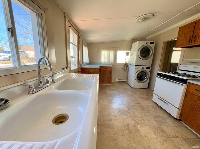 kitchen with a sink, vaulted ceiling, brown cabinets, white gas range, and stacked washer and clothes dryer