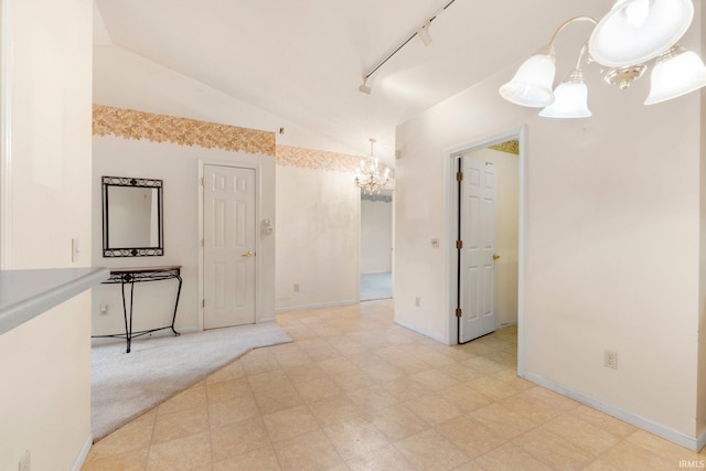 spare room with a notable chandelier, light floors, lofted ceiling, track lighting, and baseboards