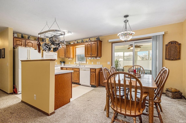 kitchen with light colored carpet, light countertops, hanging light fixtures, brown cabinetry, and white appliances