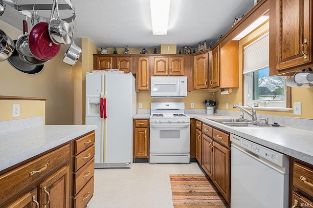 kitchen with white appliances, a sink, light countertops, brown cabinets, and light floors