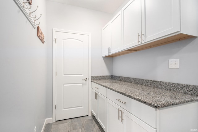 interior space featuring baseboards, light stone counters, and white cabinets