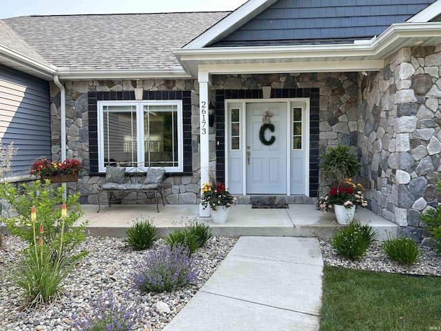 doorway to property featuring covered porch, a shingled roof, and stone siding