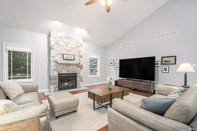 living room featuring high vaulted ceiling, visible vents, a stone fireplace, and wood finished floors