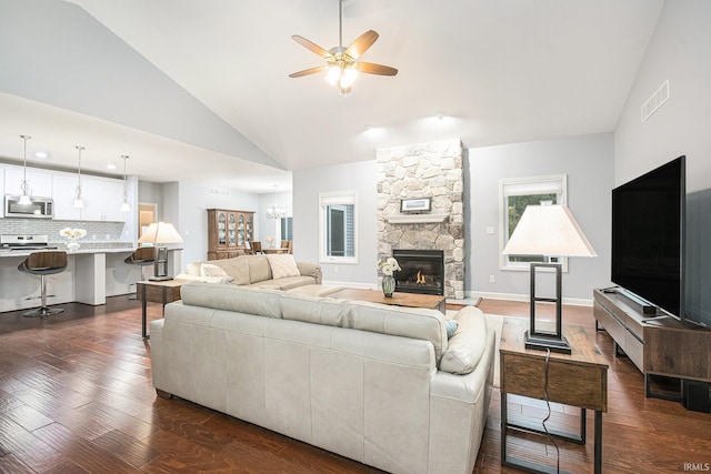 living room with high vaulted ceiling, a stone fireplace, ceiling fan with notable chandelier, dark wood-type flooring, and baseboards