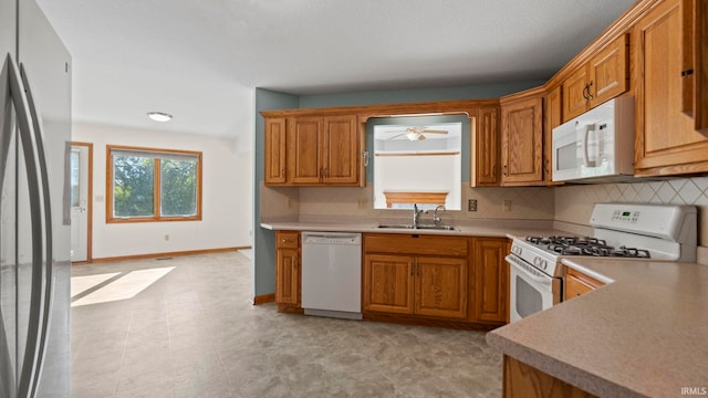 kitchen with white appliances, backsplash, brown cabinets, and a sink