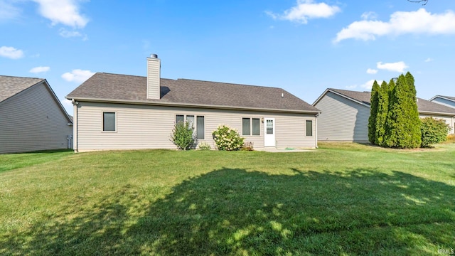 back of property featuring a shingled roof, a yard, and a chimney