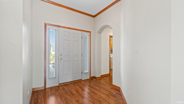 entryway with baseboards, ornamental molding, arched walkways, and wood finished floors